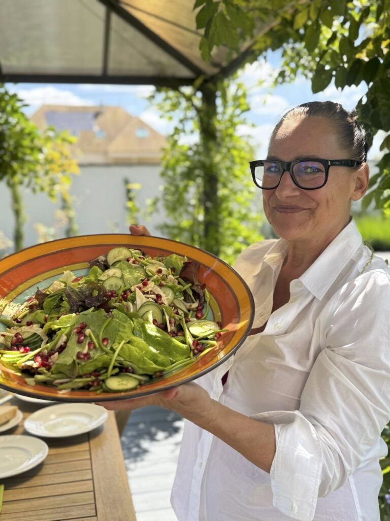 Anu holding up a big bowl of salad in the garden at Lavender House