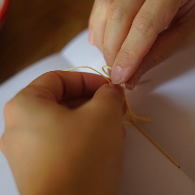 Hands stitching the spine of a notebook with yellow thread