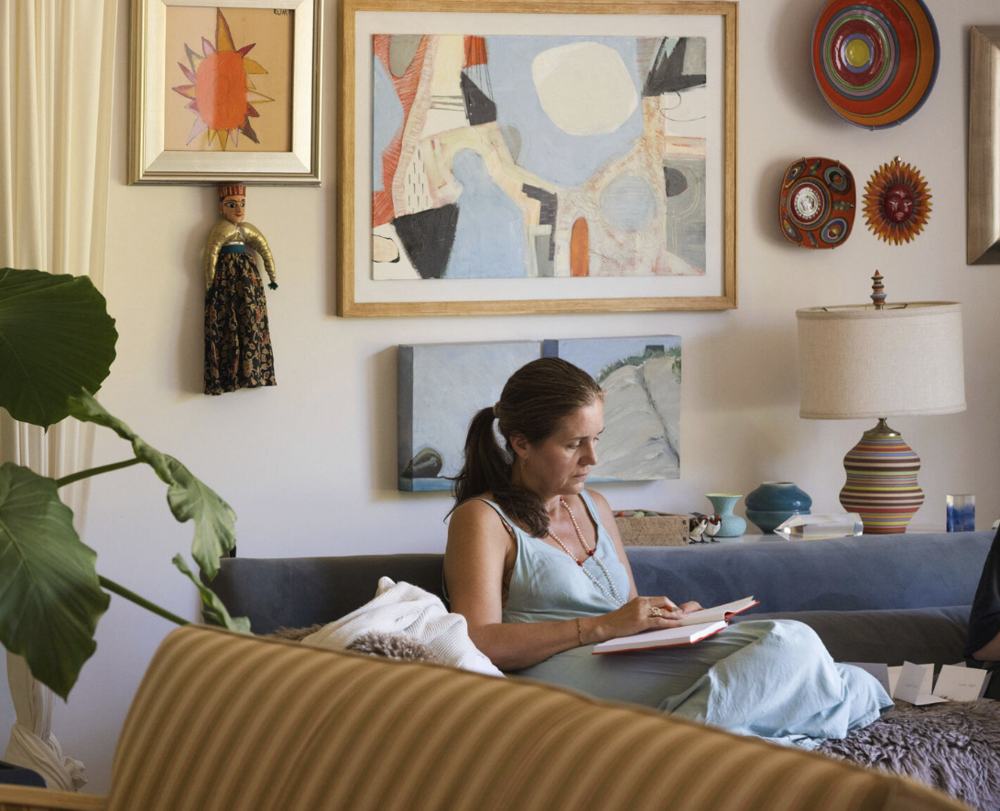 A woman writing in a journal on a sofa under a wall of paintings