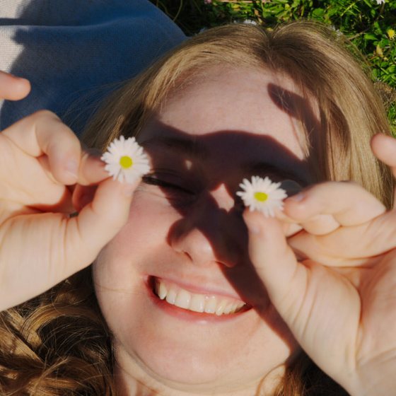 Kat lying in the grass, holding daisies over her eyes and laughing